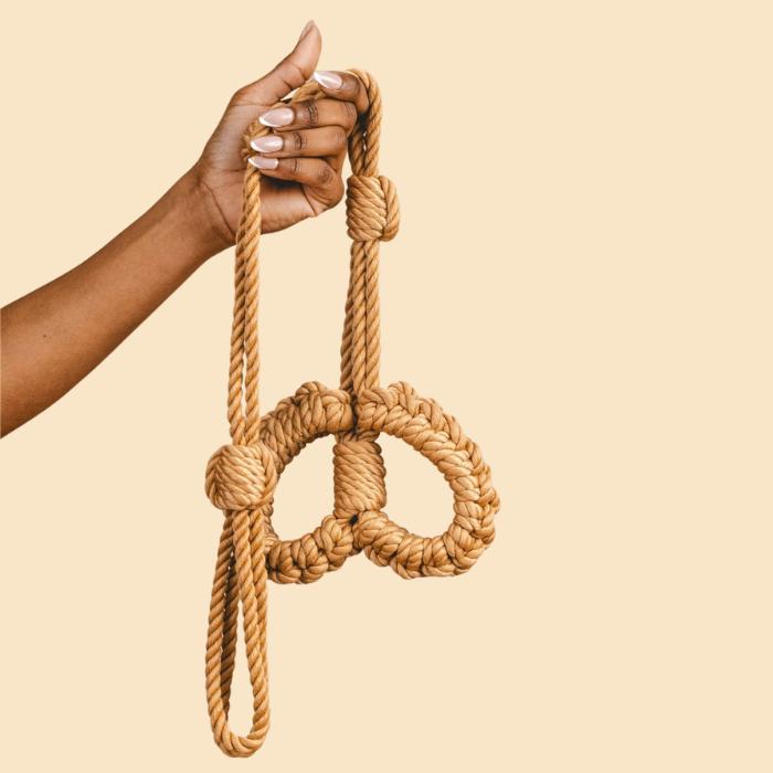 Des menottes en corde tenues dans une main.