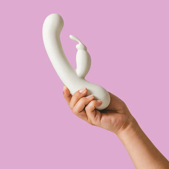 Un rabbit de couleur crème tenu en main sur fond lila.