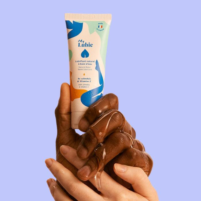 Un lubrifiant My Lubie tenu entre une main masculine et féminine avec le lubrifiant transparent coulant sur les deux mains